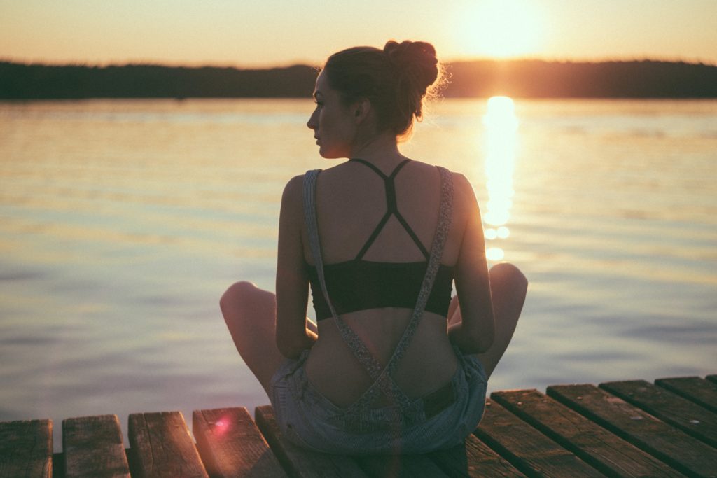 Young white woman seated on a dock at sunset, looking over the lake.